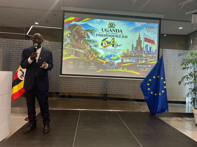 A speaker addressing the audience in front of the event banner marking 64 years of Ugandan independence